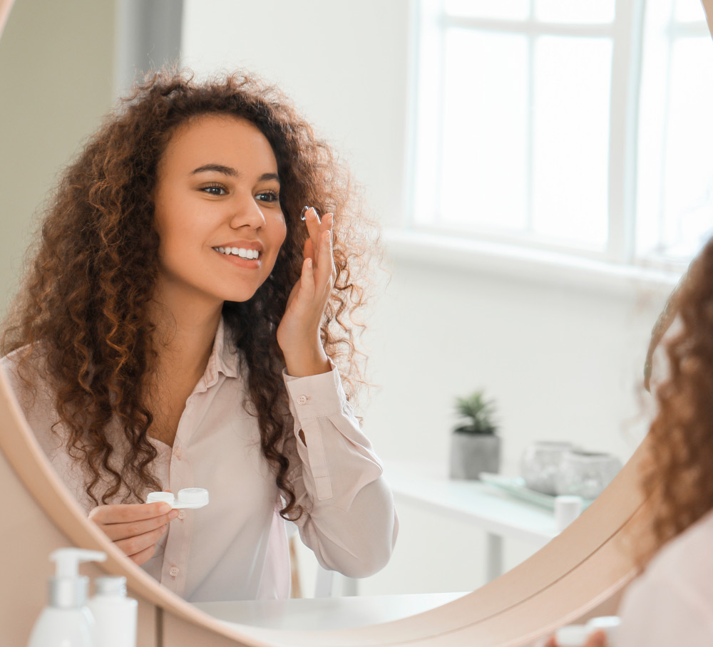 Vrouw die een contactlens indoet bij de spiegel